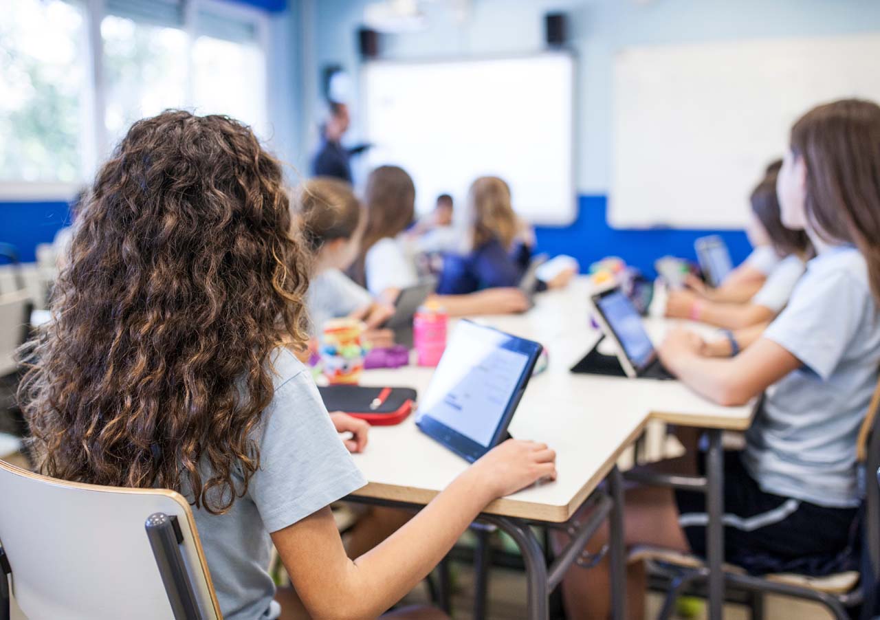 Two students in the back of the classroom with tablets following along with a classroom lesson