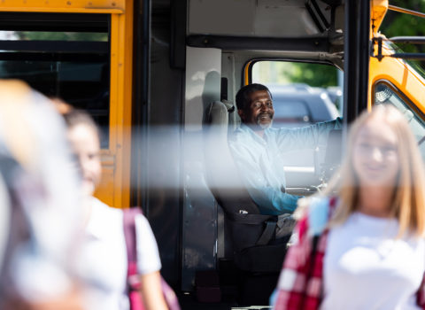 Smiling bus driver with connected custom tablet watching as students exit the bus to go home for the day