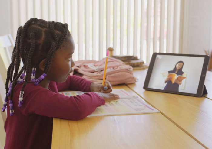 Elementary school student doing classwork remotely from home following a teacher presentation on a tablet