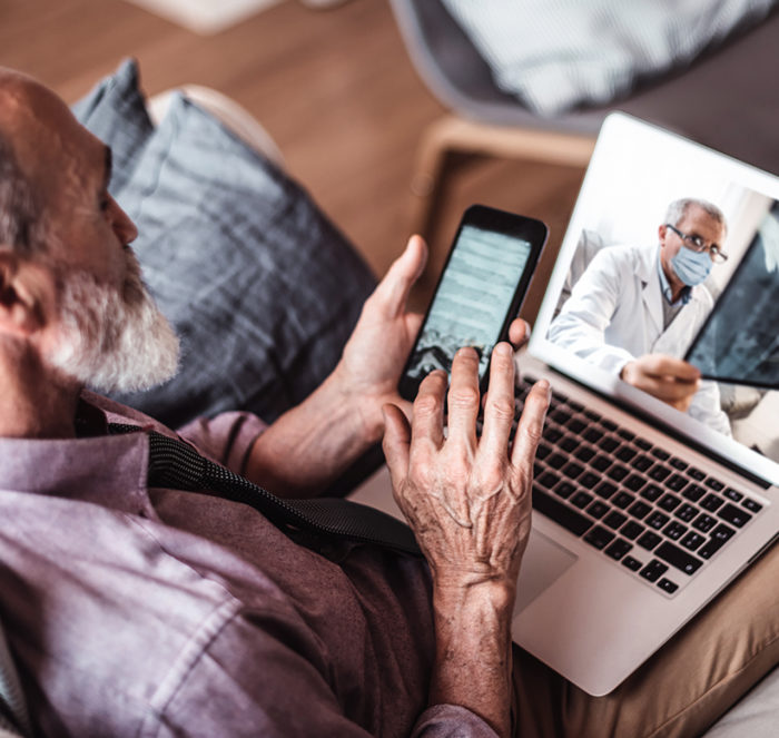 Elderly man enters information into his iphone while on a telehealth call with his doctor who is reviewing x-rays