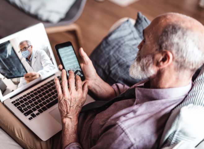 Elderly man enters information into his iphone while on a telehealth call with his doctor who is reviewing x-rays