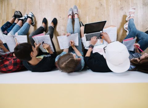 Top-down view of a row of students with backs to the wall doing a classroom assignment together