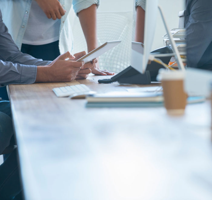 Low perspective shot of a boardroom table with colleagues collectively reviewing information on a tablet