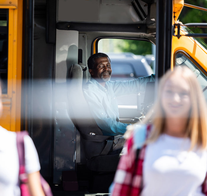 Cheerful bus driver watching at stop as children leave the bus for school