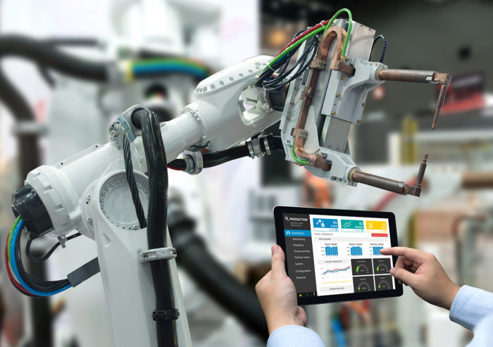Scientist monitoring performance analytics on customized connected tablet in front of a smart welding arm in a manufacturing facility