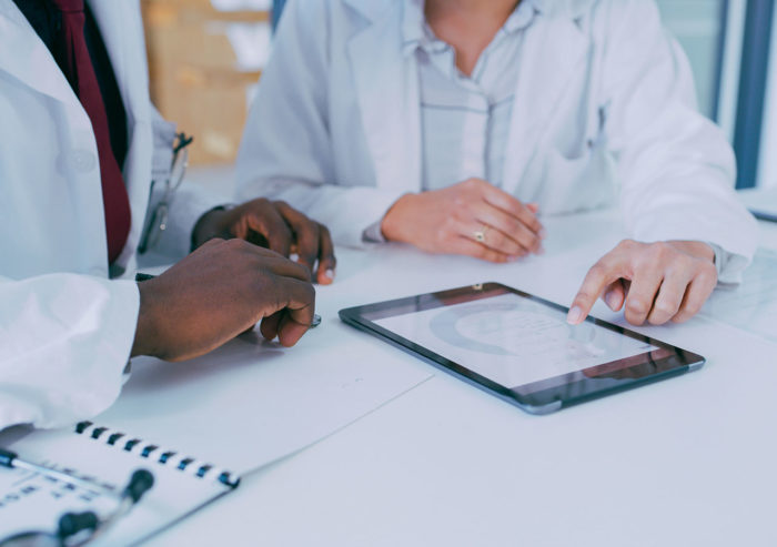 Two healthcare professionals reviewing patient information on a tablet laying flat on a desk