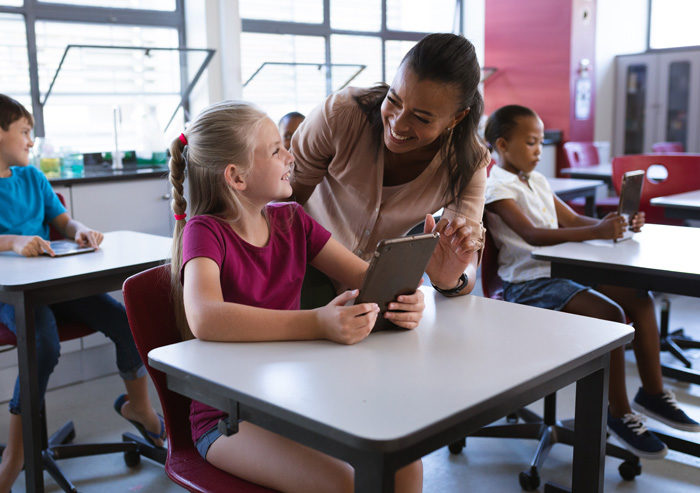 teacher collaborating with a student at her desk while looking at a tablet