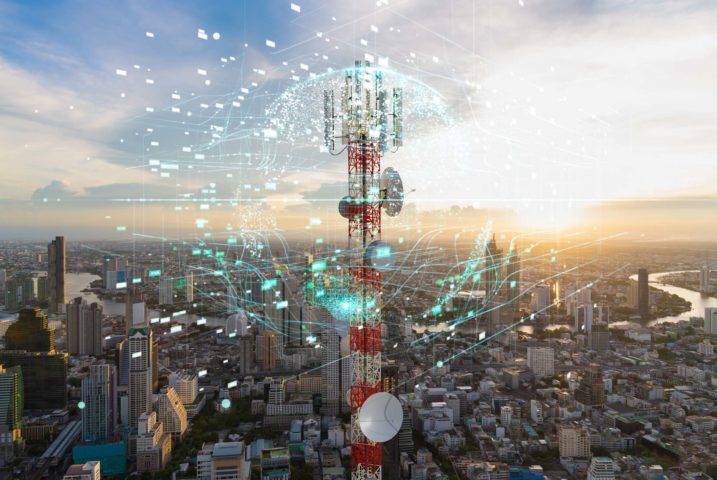 Cell tower at sunset over a major city with an overlay of connected IoT nodes to show custom connectivity