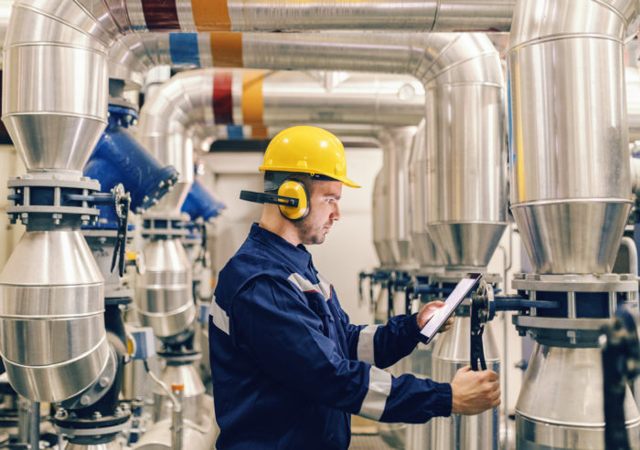 Engineer adjusting settings on a cooling unit in a boiler room with a custom tablet presenting instructions