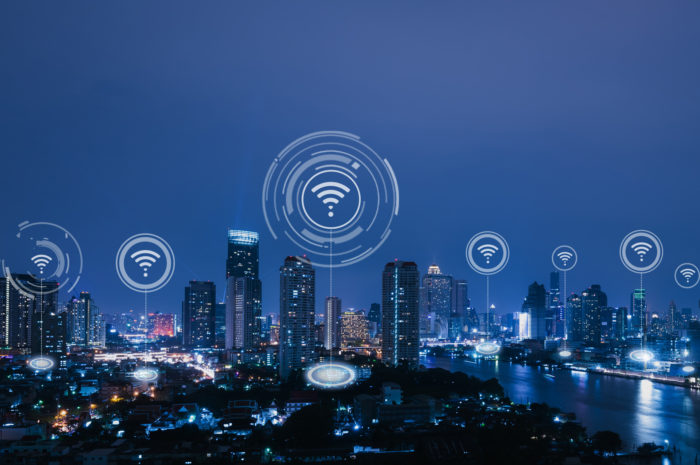 City skyline at night by river with IoT node overlay showing wireless connectivity between buildings.