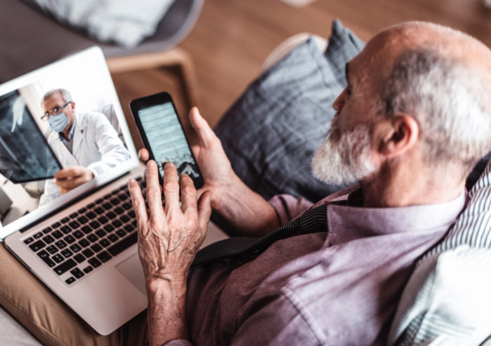 Elderly man enters information into his iphone while on a telehealth call with his doctor who is reviewing x-rays